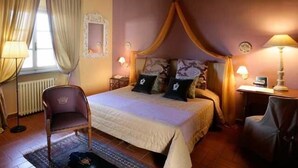 Quarto com cama, cadeira, mesa de cabeceira e abajur.