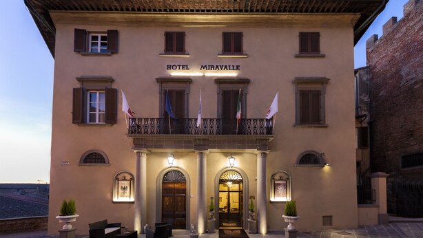 Um hotel chamado "HOTEL MIRAVALLE", com fachada clássica, entrada em arco e uma varanda com bandeiras.