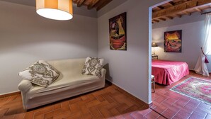 Um quarto aconchegante com sofá, cama com colcha vermelha e obras de arte nas paredes.