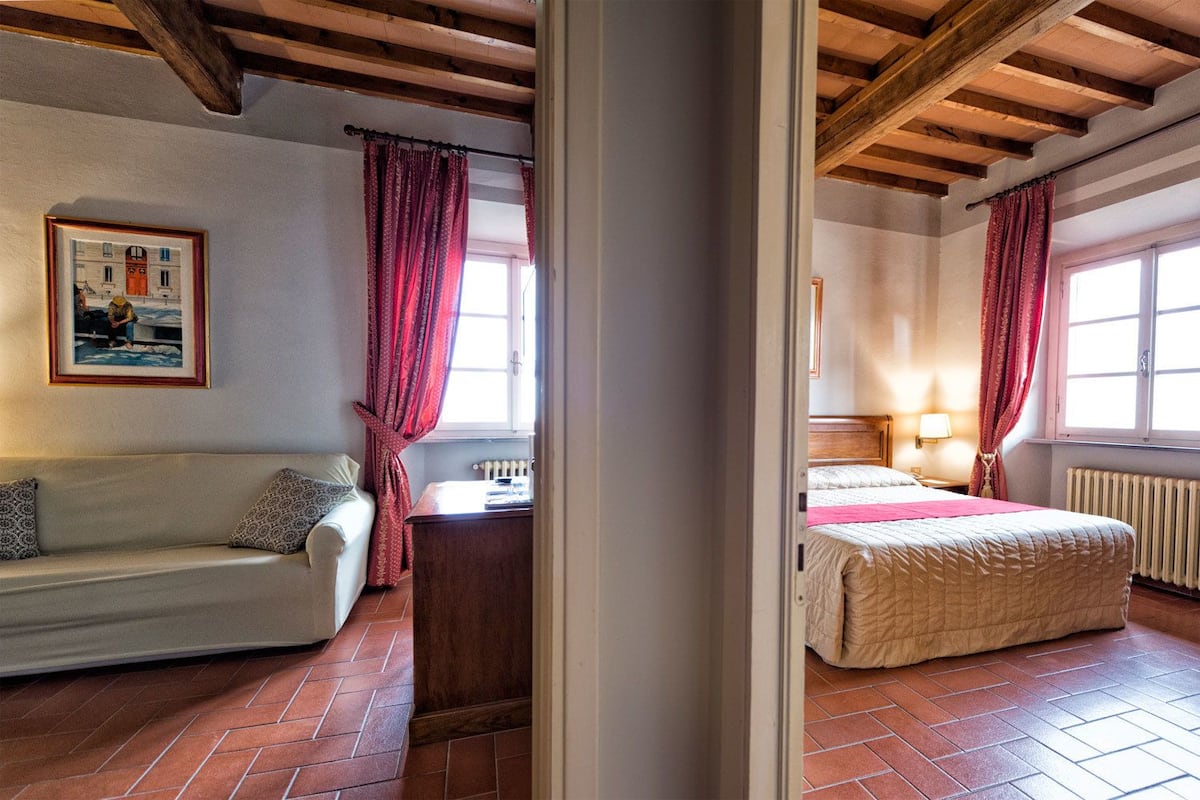 A room with a bed, a sofa, a radiator, and a window with curtains.