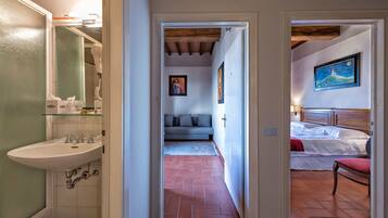 Habitación de hotel con cama, piso de baldosas rojas, sofá gris y un cuadro en la pared.