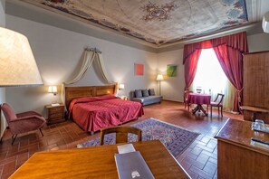 A hotel room with a large bed, a desk with a laptop, a small sofa, a dining table, and a view of the outdoors. - Hotel Miravalle (San Miniato)