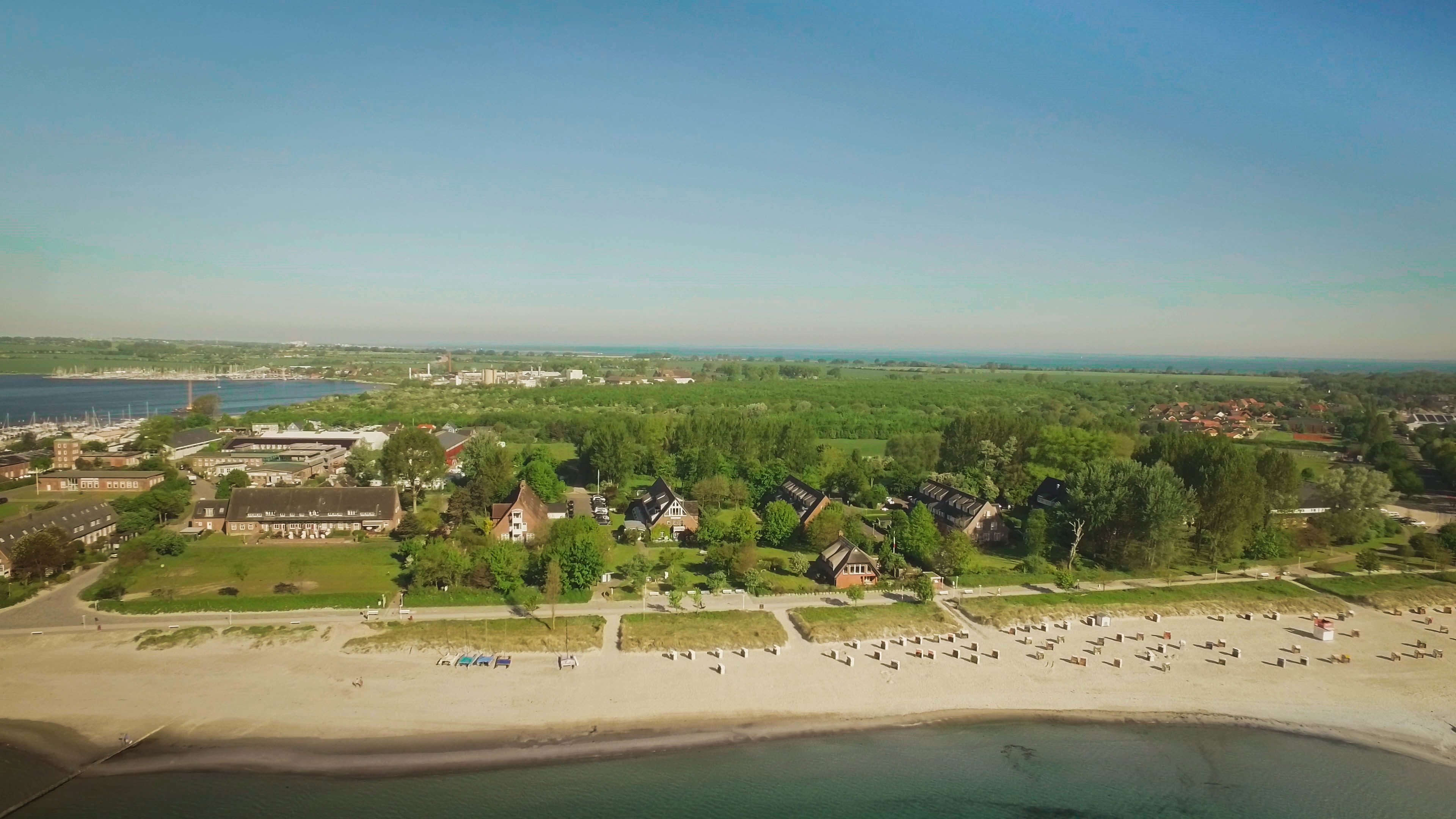 Luchtbeeld van een kustgebied met een zandstrand, woongebouwen en een jachthaven.