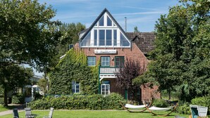 A hotel with a brick facade, large windows, and a well-maintained lawn with outdoor seating. - Hotel am Wind (Grossenbrode)