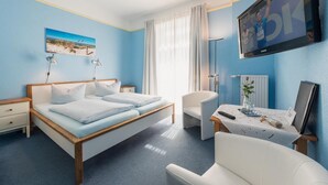 A bedroom with a bed, bedside tables, a desk, a chair, a TV, and a window with curtains. - Hotel am Wind (Grossenbrode)