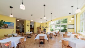 A dining area with multiple tables and chairs, wooden flooring, and pendant lighting. - Hotel am Wind (Grossenbrode)