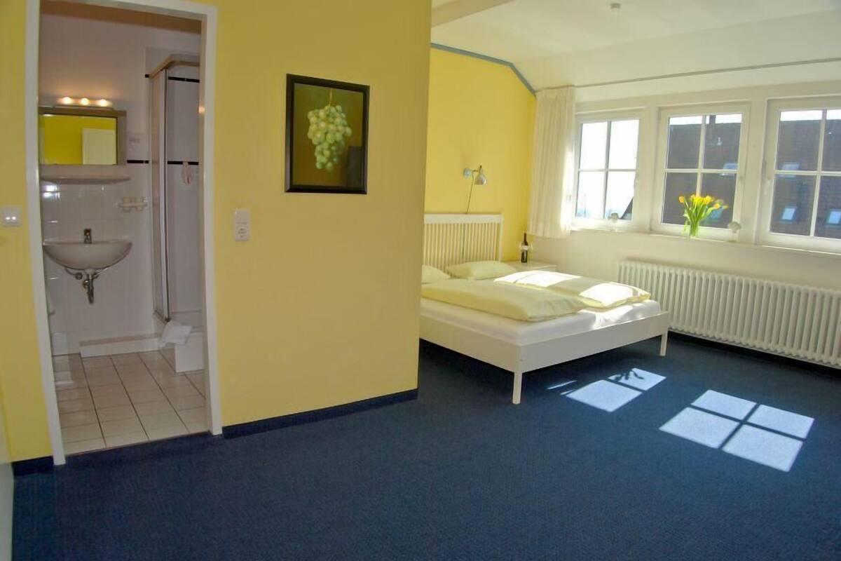 Ein Schlafzimmer mit Bett, einem Fenster mit Blick, einem Heizkörper und einem Badezimmer mit Waschbecken.