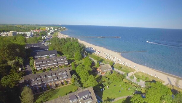 An aerial view of a coastal area with a beach, residential buildings, and a park. - Hotel am Wind (Grossenbrode)