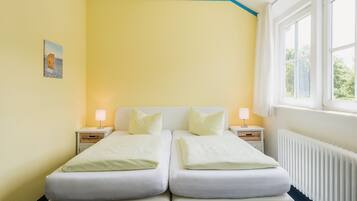 A double bed with two pillows, a bedside table with a lamp, and a window with curtains.
