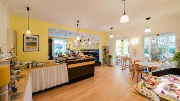 A bright and airy breakfast area with a buffet setup, wooden flooring, and pendant lighting.