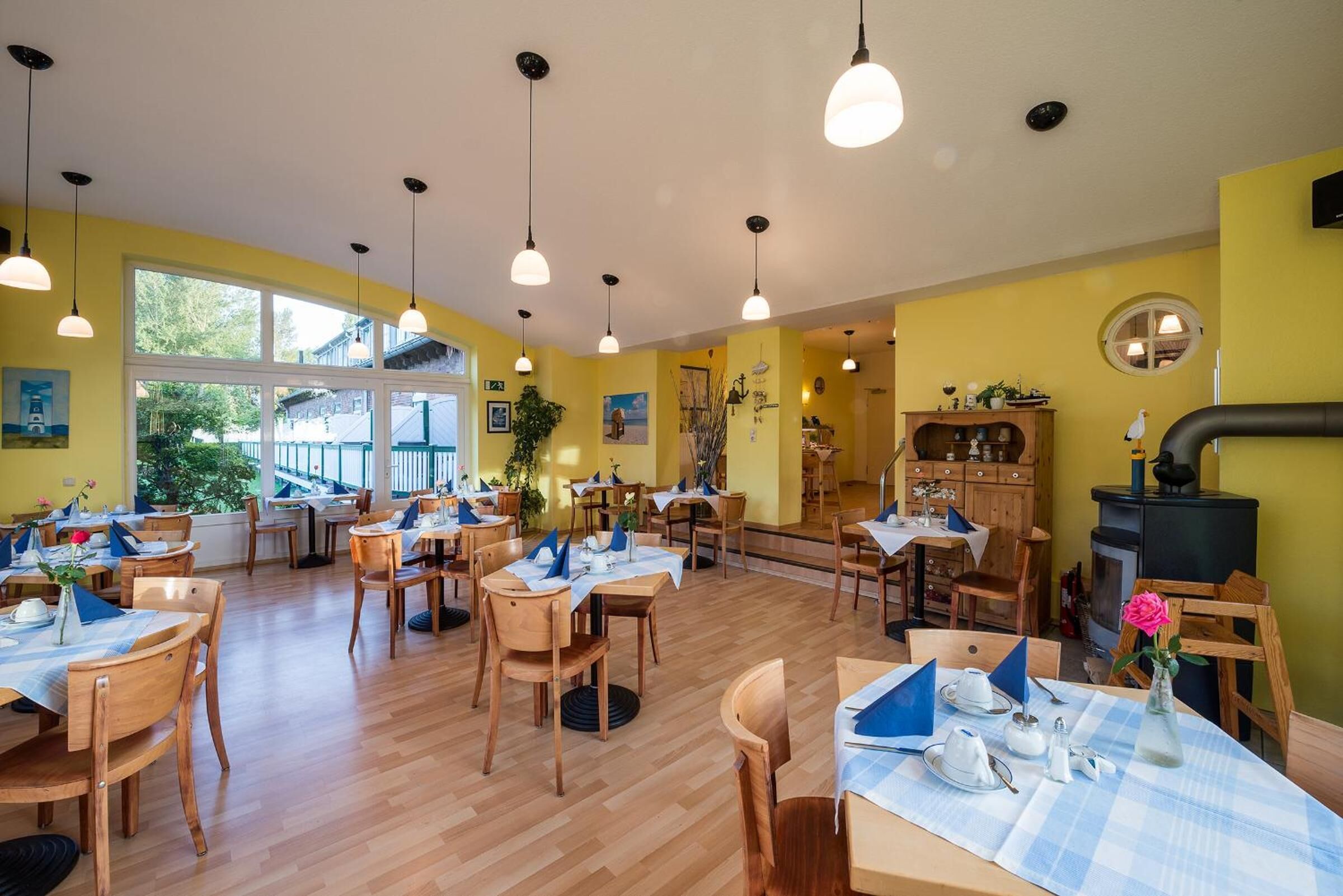A restaurant with wooden tables and chairs, hanging pendant lights, and yellow walls.