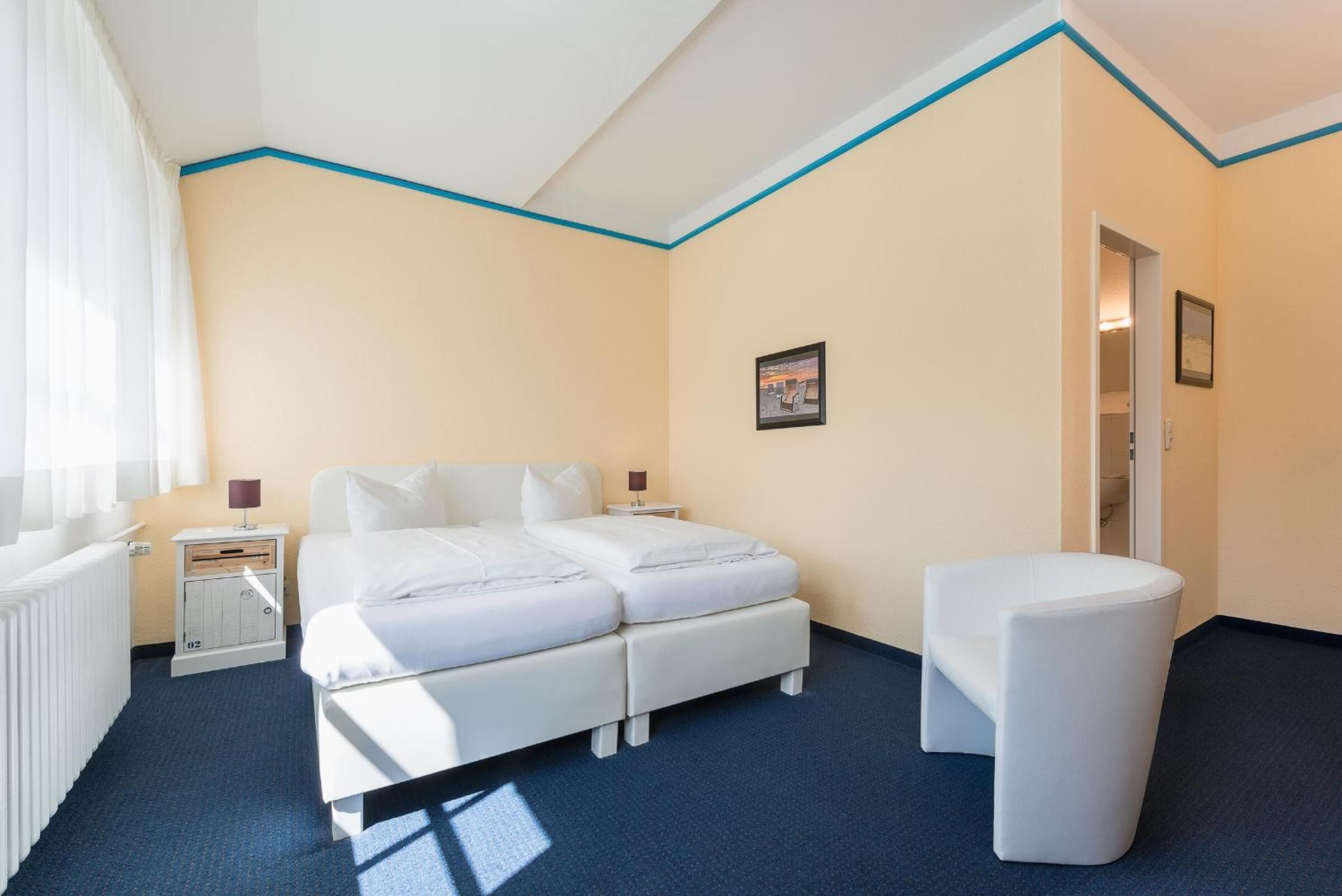 Una habitación de hotel con cama, mesitas de noche, una silla y un radiador.