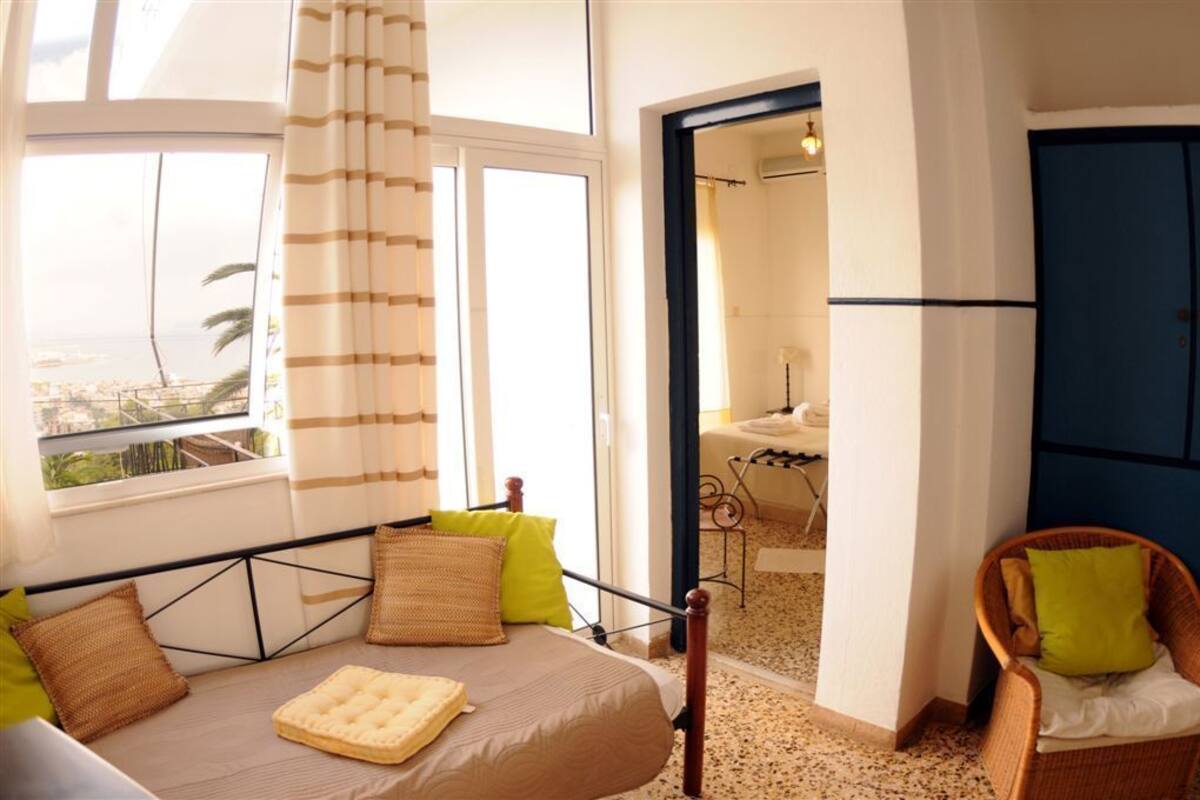 Un dormitorio con cama, ventana con cortinas, una silla y vista a la playa.