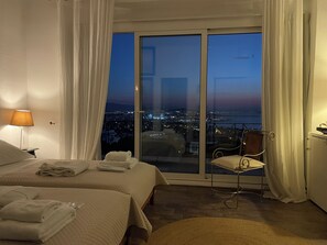 A hotel room with a large sliding glass door to the outside, a bed with neatly folded towels, a chair, and a lamp. - Hotel Akrotiri (Chania)