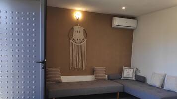 Uma sala de estar moderna com um sofá seccional cinza, um enfeite de macramé na parede e um aparelho de ar condicionado.