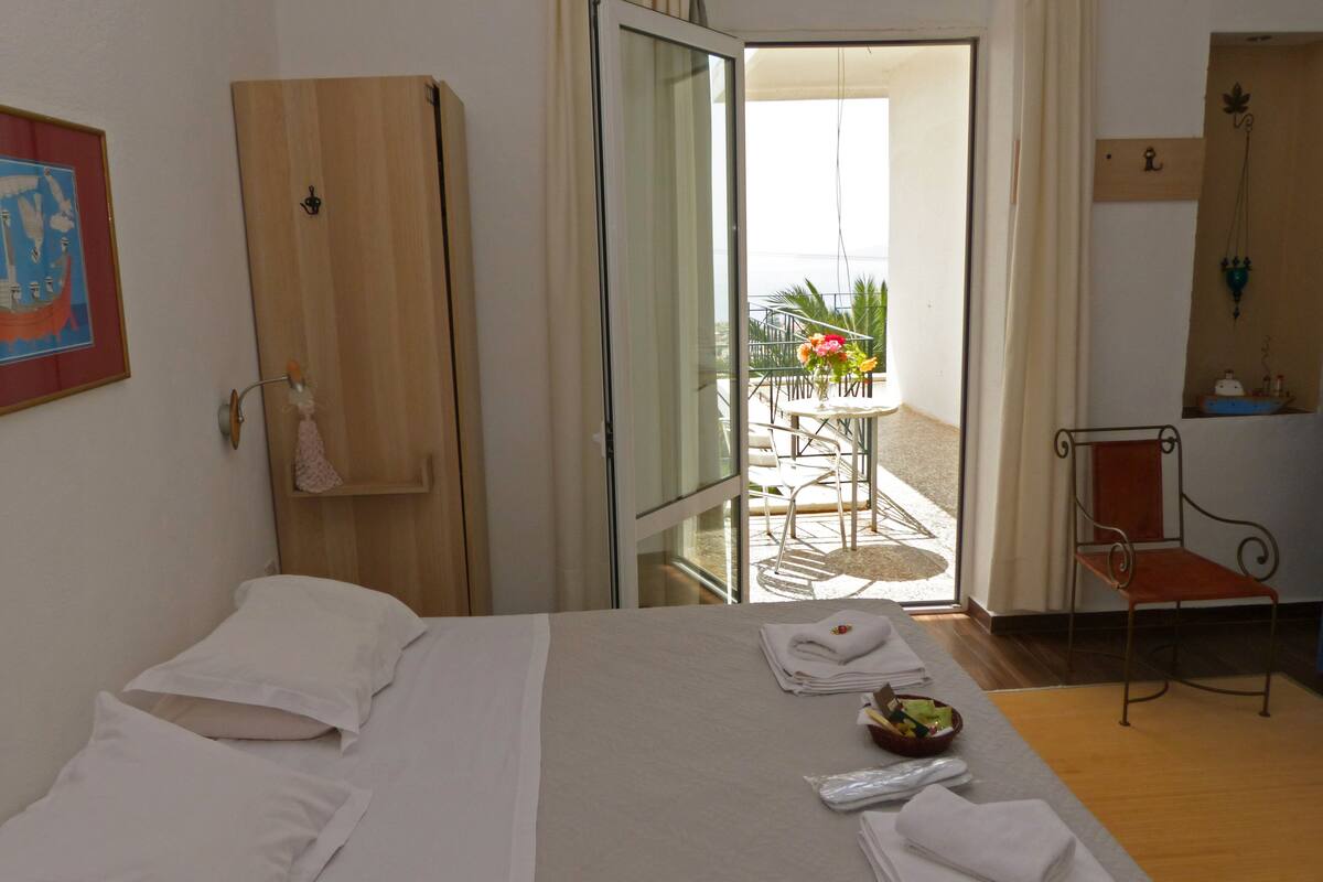 Habitación de hotel con cama, armario de madera, escritorio con silla y balcón con mesa y sillas.