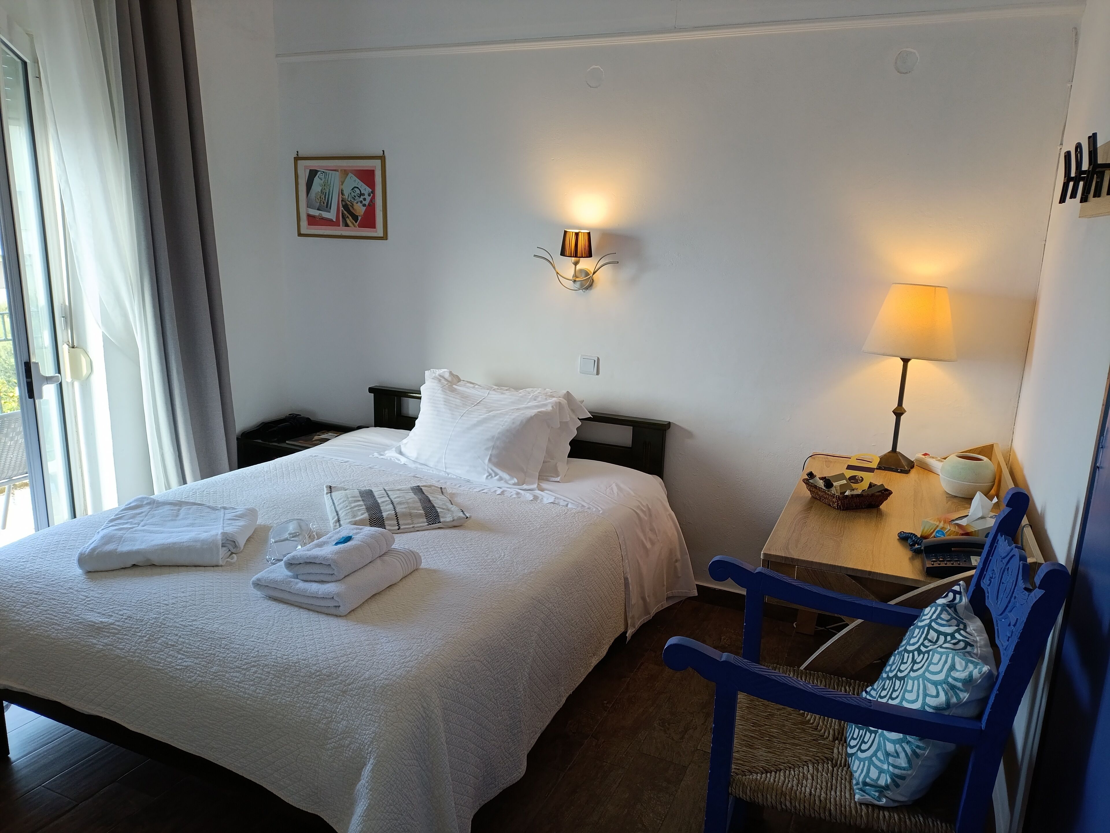 A neatly made bed with white linens, a bedside lamp, and a chair with a woven seat.