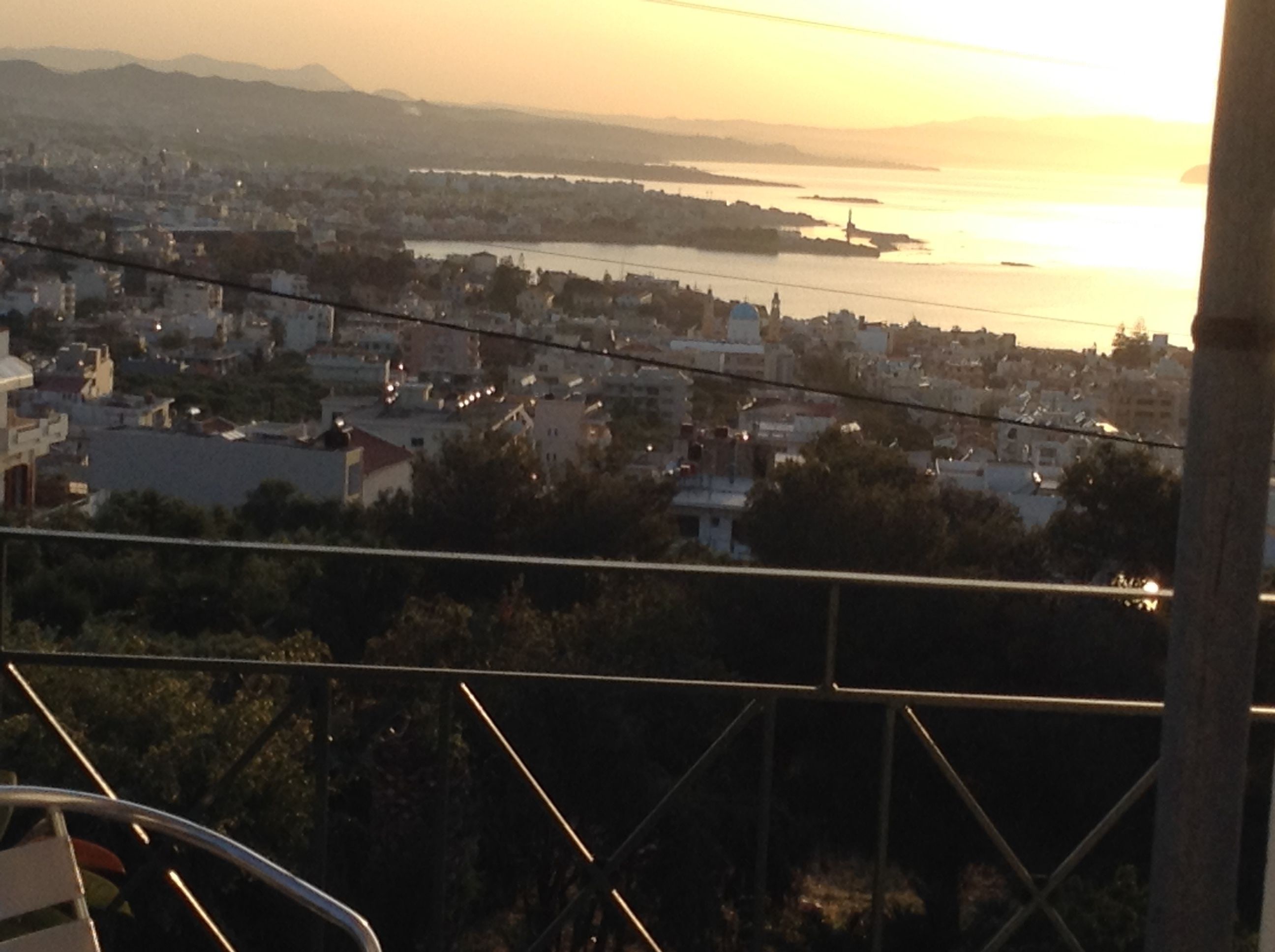 A cityscape at sunset with buildings and a body of water in the distance.