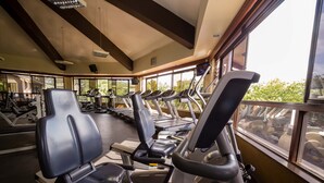 Ein Fitnessstudio mit mehreren Laufbändern und Trainingsgeräten, großen Fenstern und einer hohen Decke mit freiliegenden Balken.