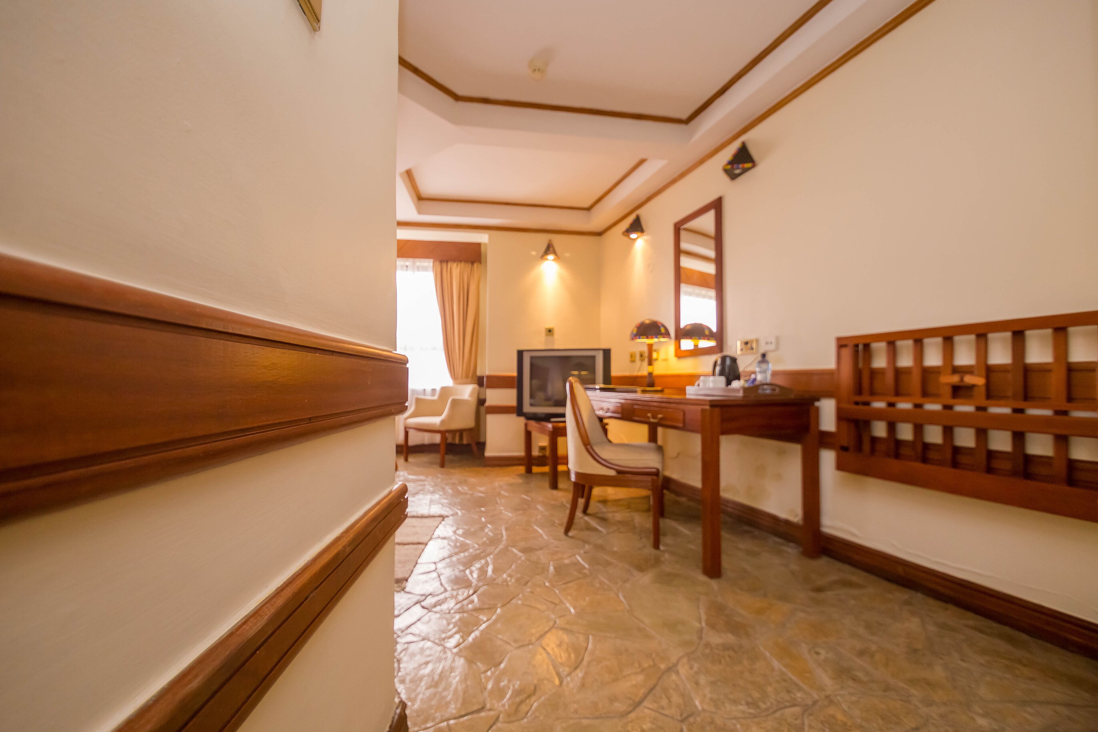 A hotel room with a stone floor, wooden furniture, a television, and a mirror on the wall.