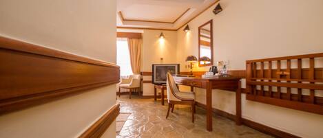 Quarto de hotel com piso de pedra, móveis de madeira, televisão e espelho na parede.