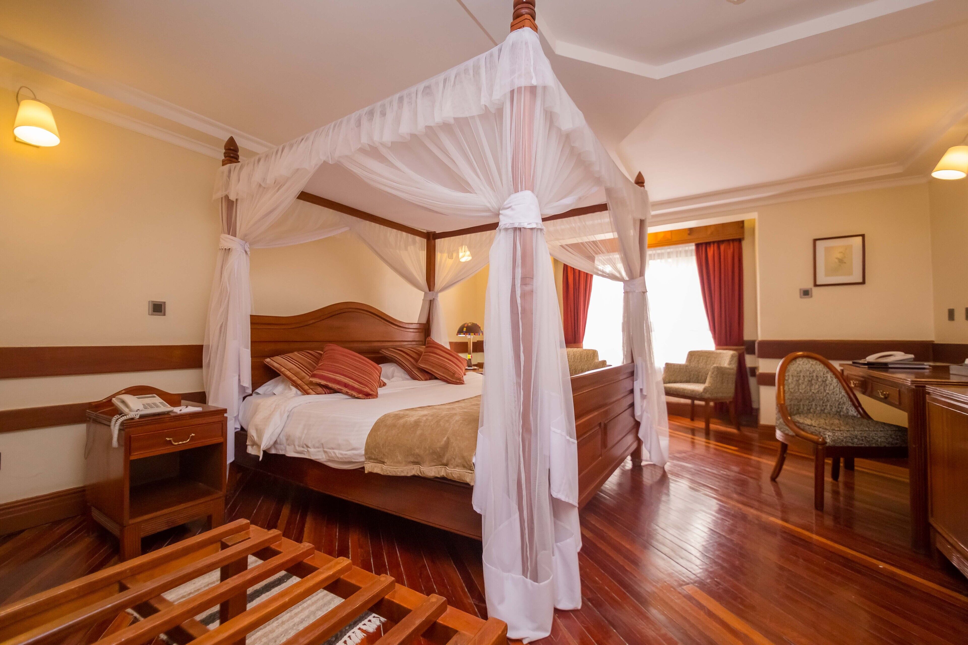 A four-poster canopy bed with a wooden headboard, bedside tables, and a desk with a chair.