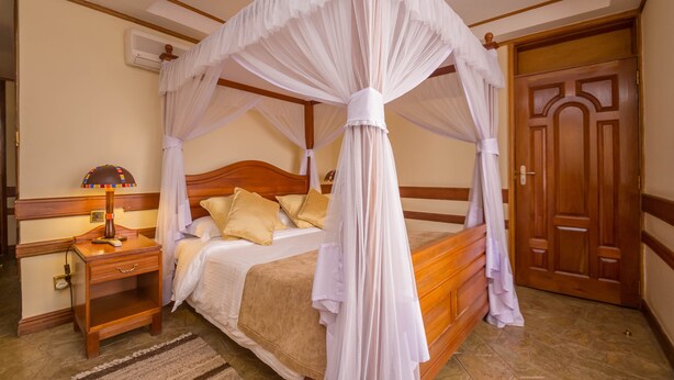 Ein Schlafzimmer mit einem Himmelsbett, einem Holzkopfende, einem Nachttisch mit Lampe und einem Kleiderschrank.