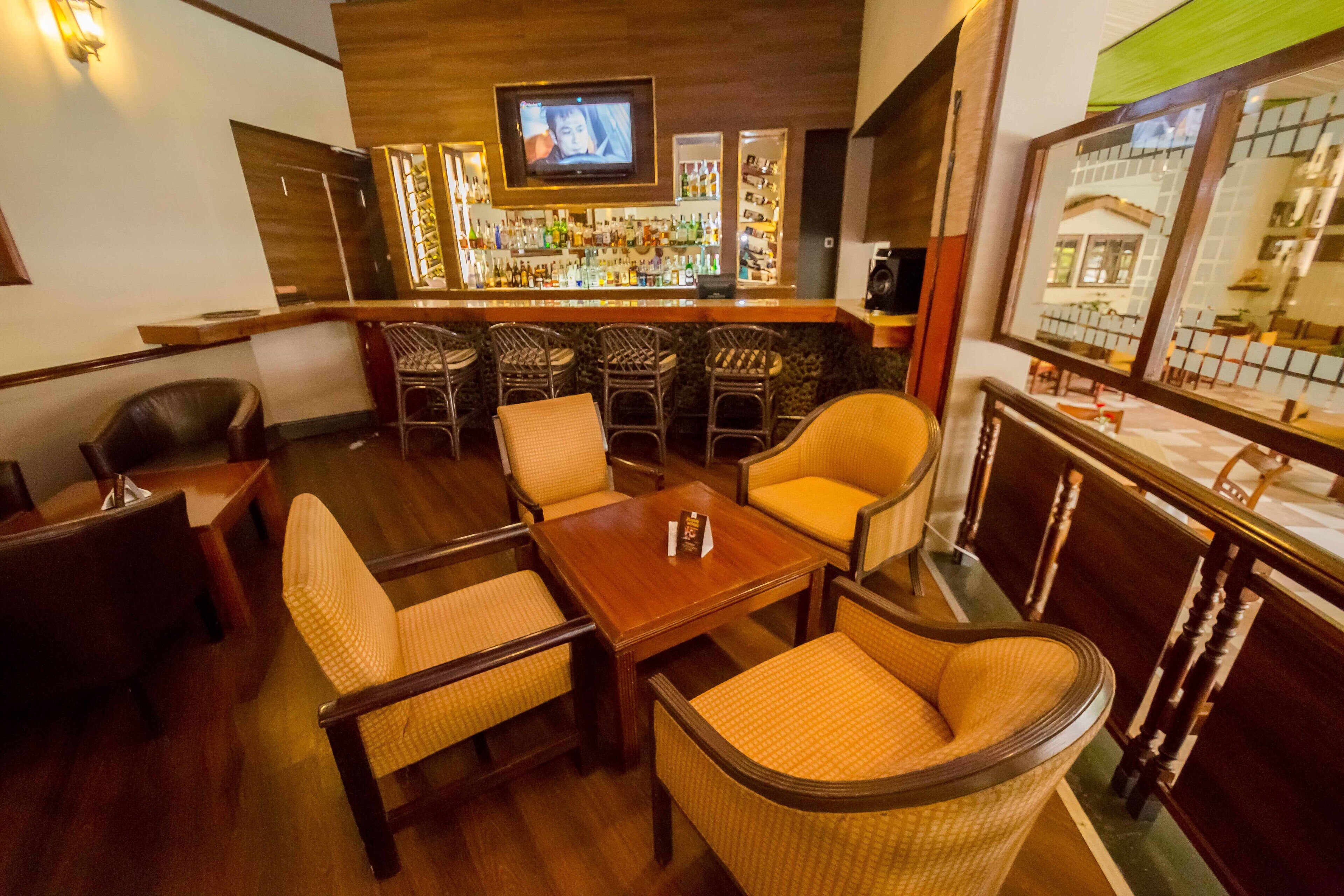 A bar area with wicker chairs, a wooden table, and a television mounted above the bar.