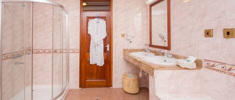 A modern bathroom with a glass-enclosed shower, a wooden door leading to a walk-in closet, and a vanity with a sink and mirror.