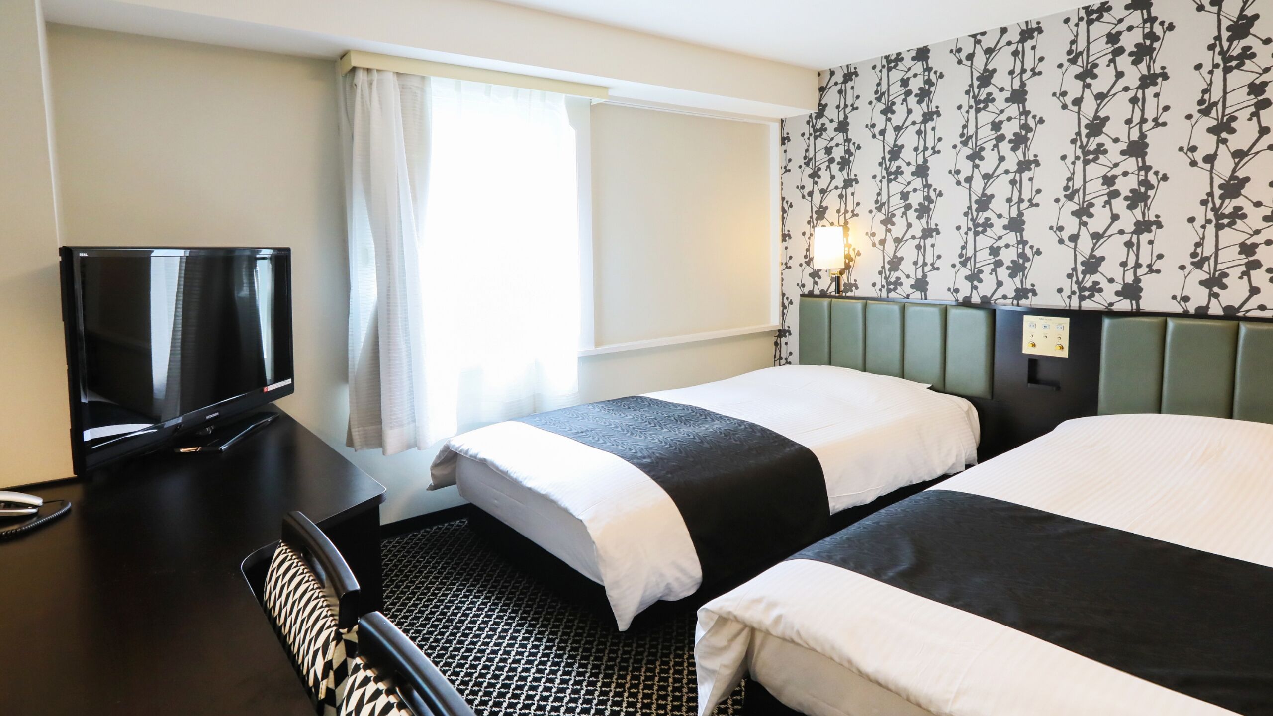 Ett hotellrum med två sängar, en tv, ett skrivbord och en vägg med ett mönster.