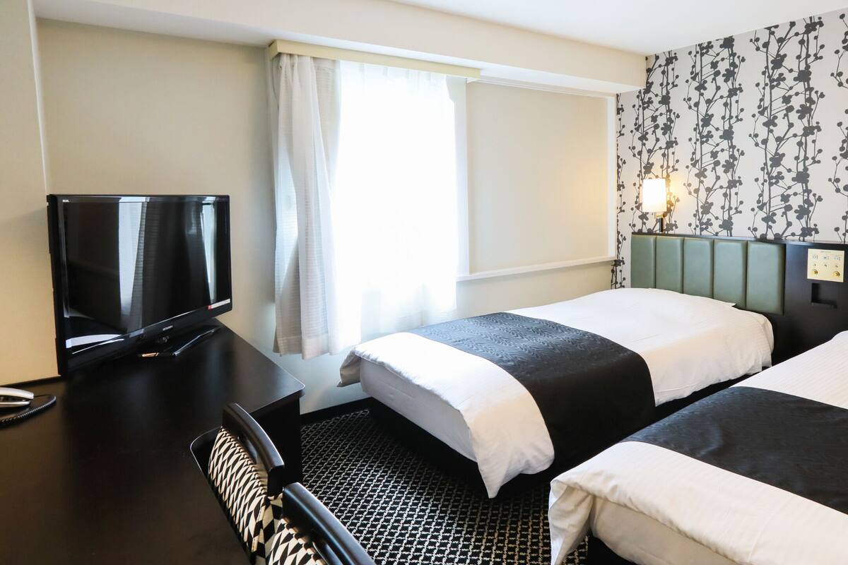 Habitación de hotel con dos camas, televisión, escritorio y pared con estampado.