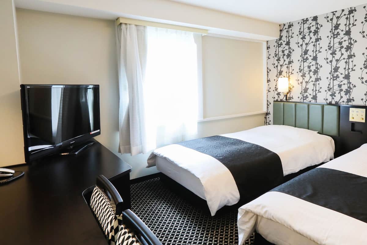 Hotellihuone, jossa on kaksi sänkyä, televisio, työpöytä ja kuviollinen seinä.