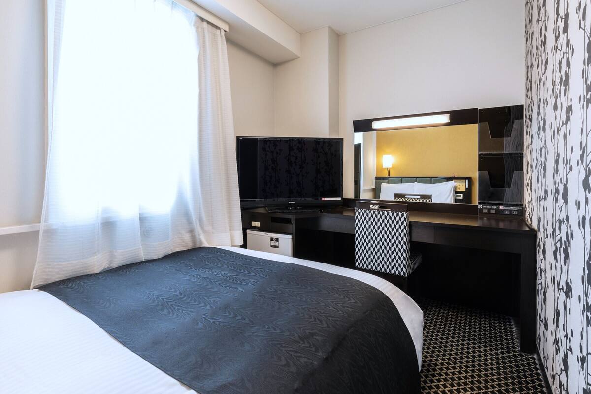 Una habitación de hotel con una cama, un escritorio, un televisor y un espejo.