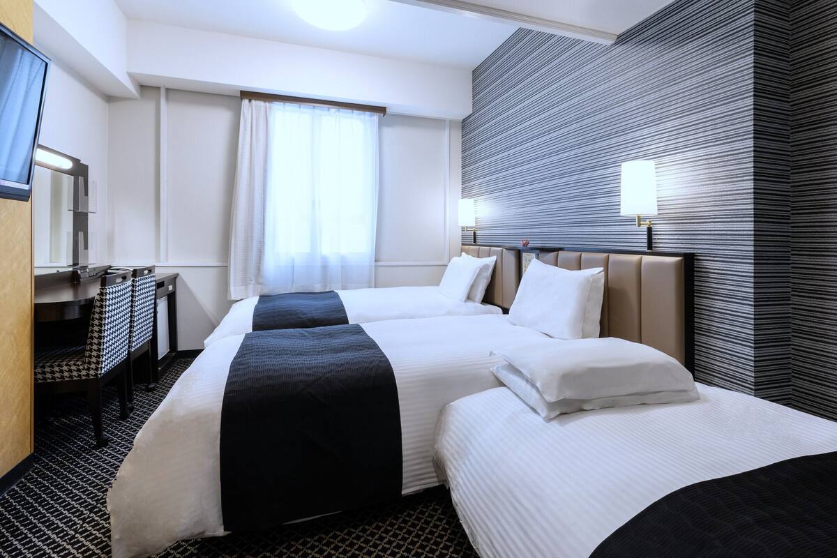 Una habitación de hotel con dos camas, un escritorio, un espejo y una ventana con cortinas.