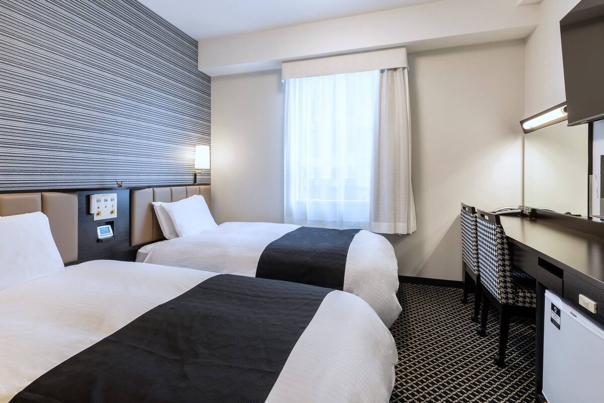 Habitación de hotel con dos camas, un escritorio, un espejo y un panel de control.