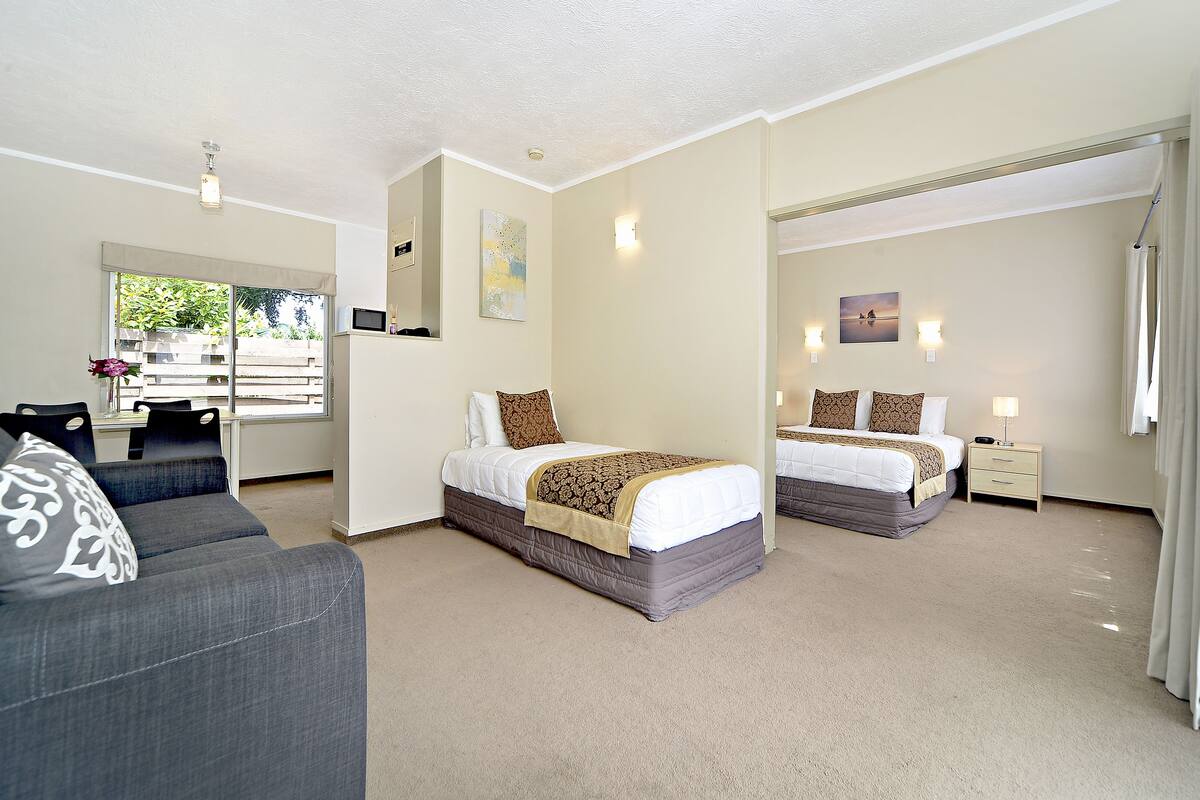 A hotel room with two beds, a sofa, a desk, and a view of the outdoors.