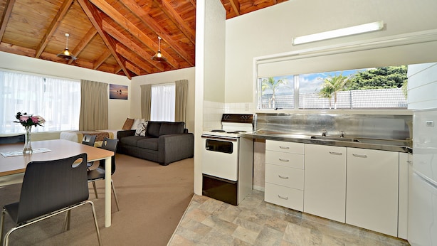 A modern kitchen with white cabinets, a stainless steel sink, and a large window overlooking a garden. - Takapuna Motor Lodge (Auckland)
