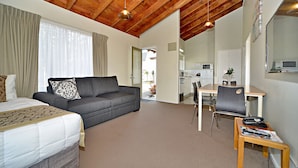 A hotel room with a bed, a grey sofa, a wooden ceiling, a dining area, and a small table with a magazine and a phone. - Takapuna Motor Lodge (Auckland)
