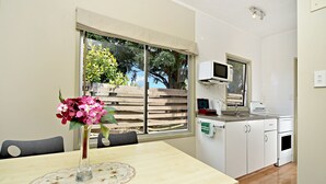 A dining area with a table set for two, a vase with flowers, and a view of the garden through a window. - Takapuna Motor Lodge (Auckland)