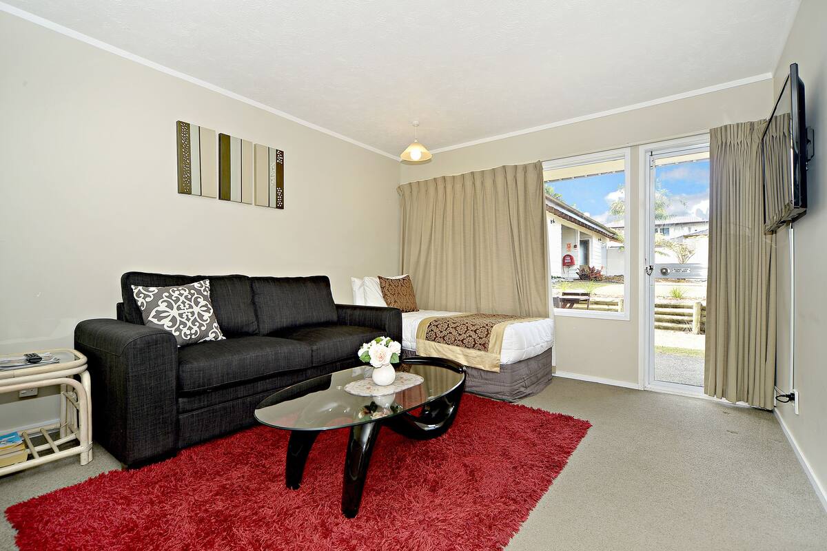 A modern living room with a black sofa, a glass coffee table, and a red rug.