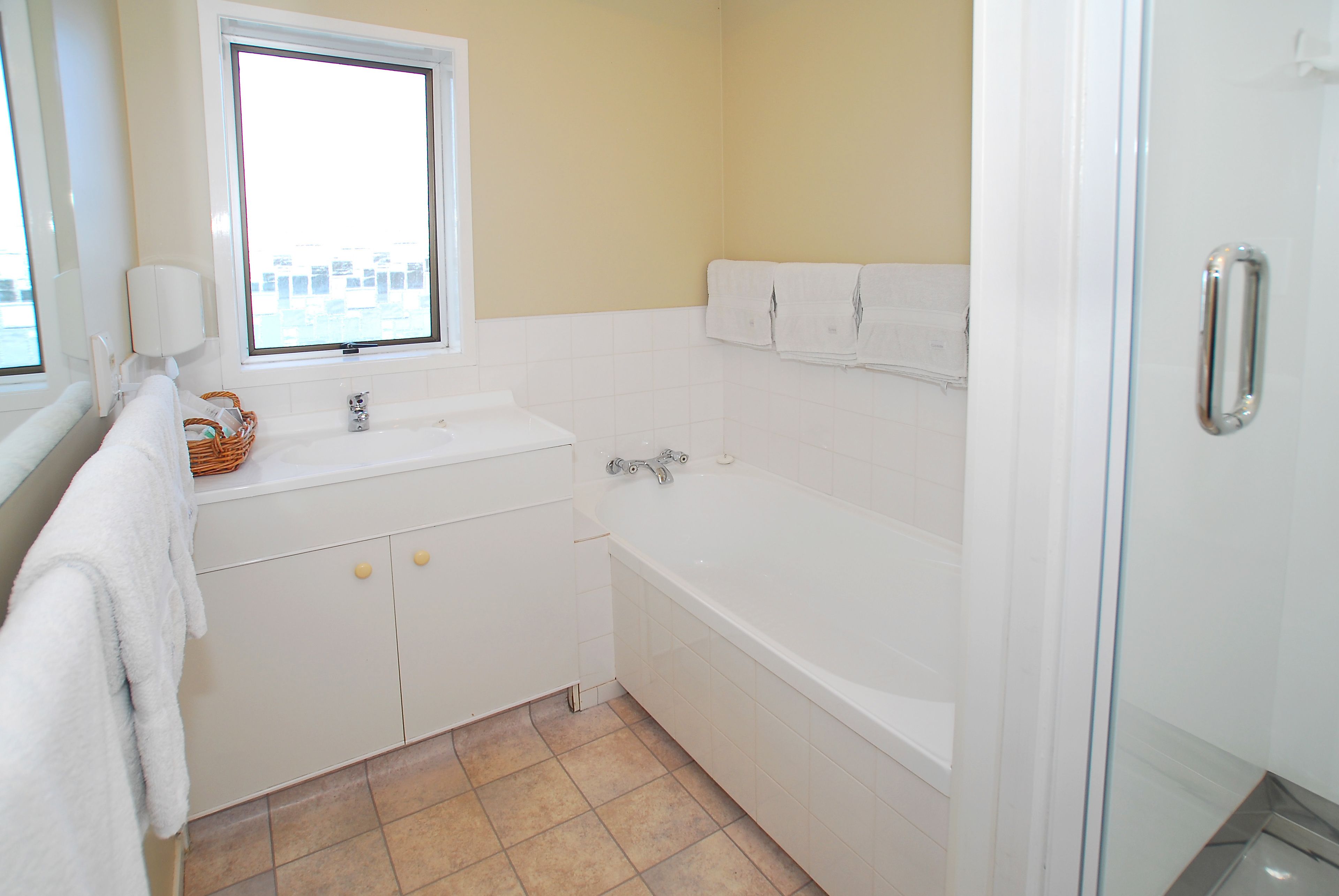 A bathroom with a bathtub, a window, a sink, and a shower.
