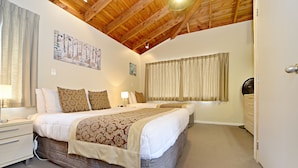 A bedroom with two beds, wooden ceiling beams, a large window with curtains, and a bedside table with a lamp. - Takapuna Motor Lodge (Auckland)