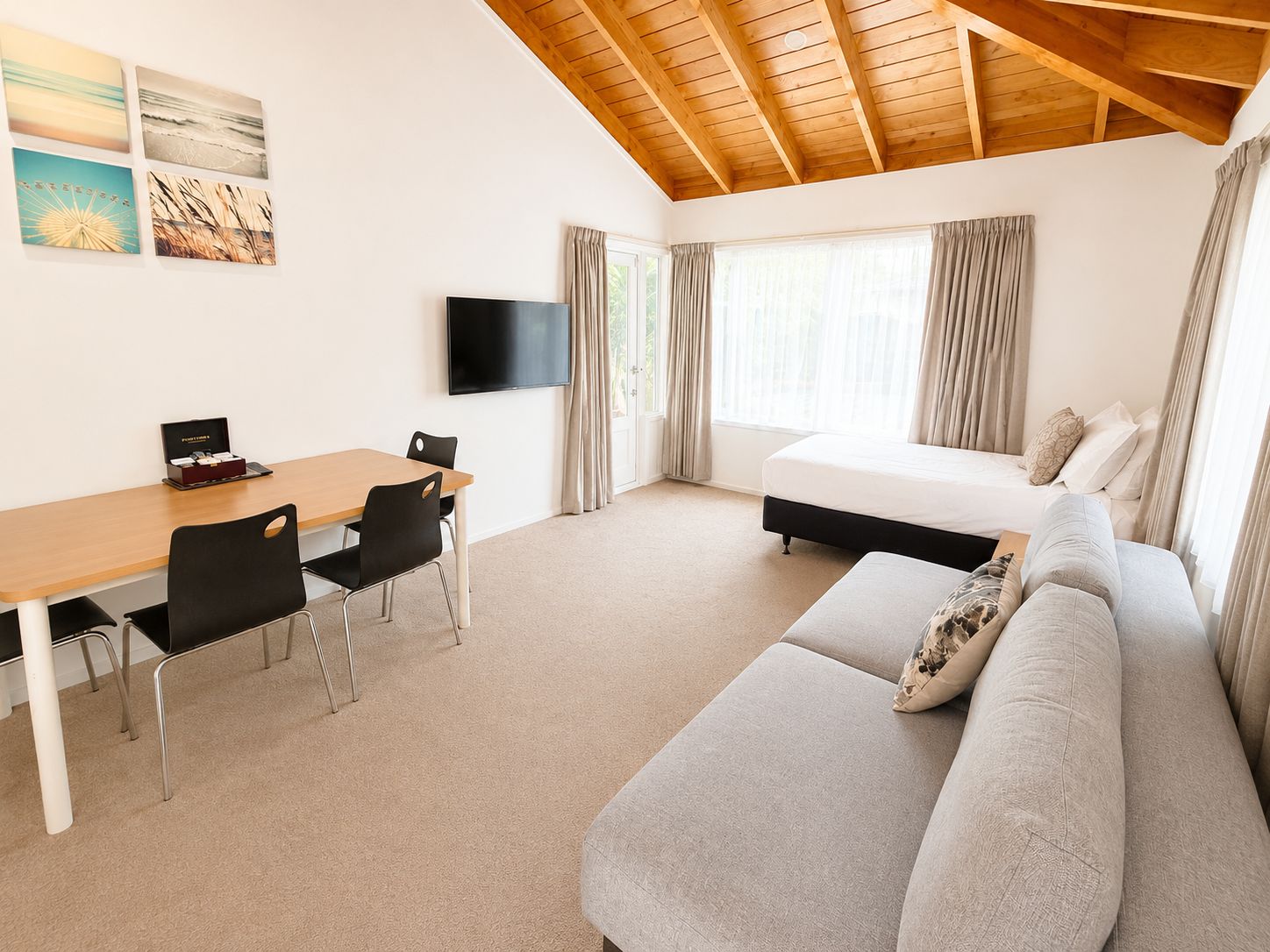 Una habitación con cama, sofá, escritorio con sillas, televisión de pantalla plana y ventana con cortinas.
