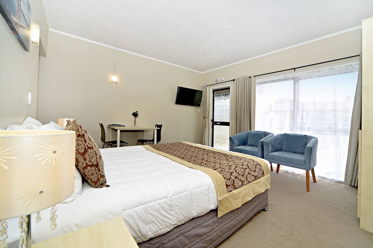 A hotel room with a bed, a desk, a television, and two chairs.