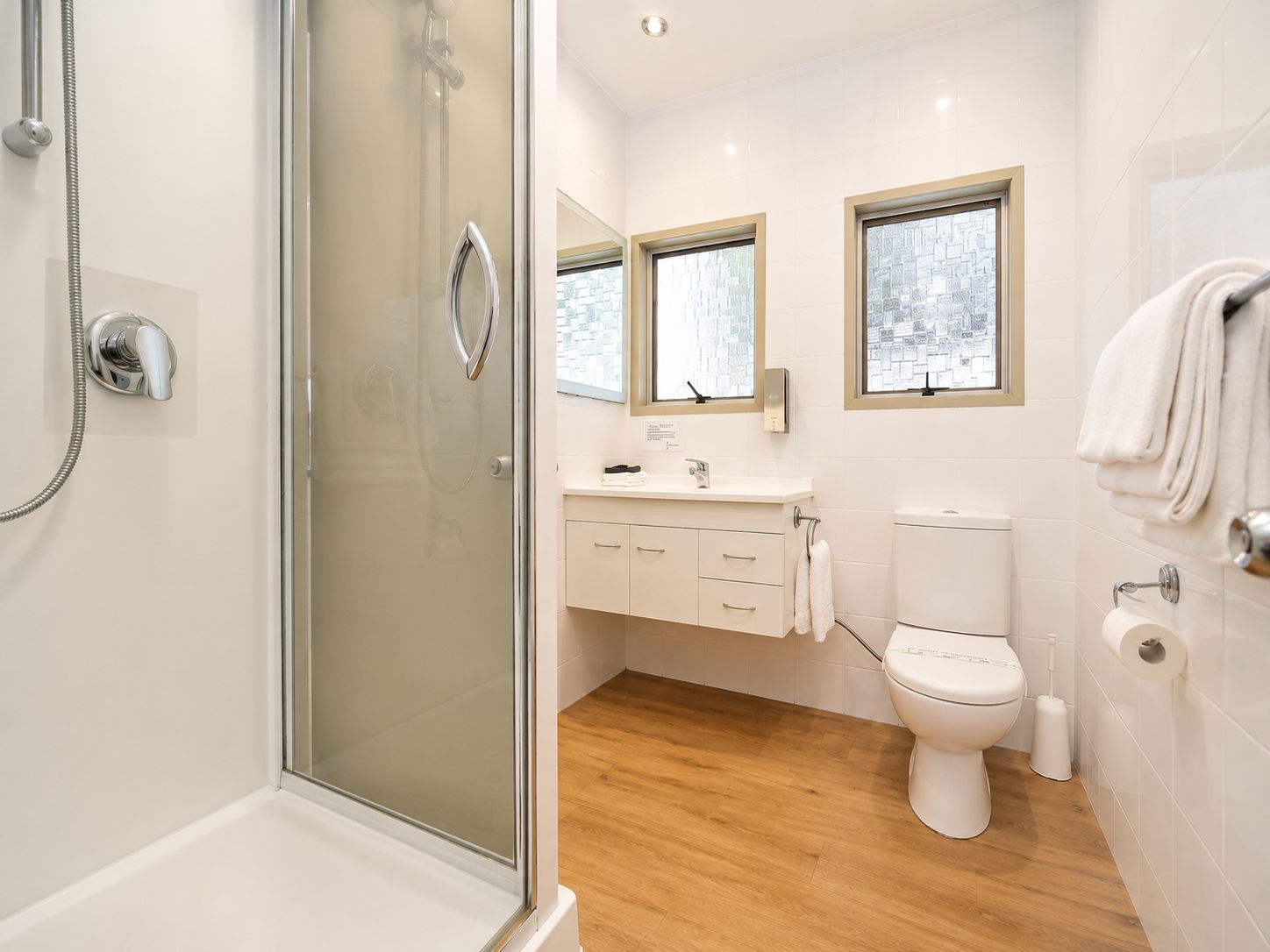 A modern bathroom with a glass shower enclosure, a toilet, a sink with a mirror, and a window.
