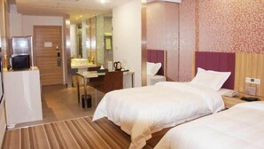 Een hotelkamer met twee bedden, een bureau, een televisie en een badkamer zichtbaar door een glazen deur.