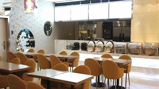 Een moderne eetruimte met tafels en stoelen, een keuken op de achtergrond en een decoratieve wand met een ronde spiegel.