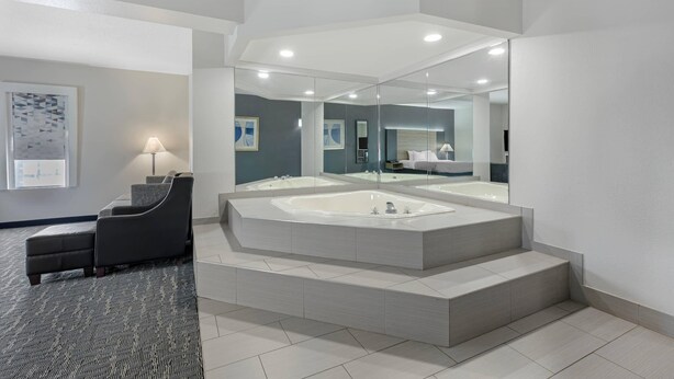 Un baño moderno con un espejo grande, una bañera independiente y una zona de estar con una lámpara.