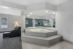 Un baño moderno con un espejo grande, una bañera independiente y una zona de estar con una lámpara.