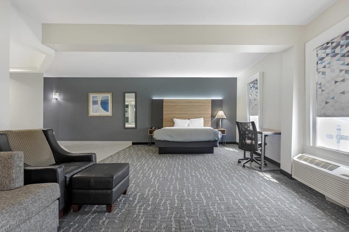 A hotel room with a bed, a desk, a chair, a sofa, and a large window.